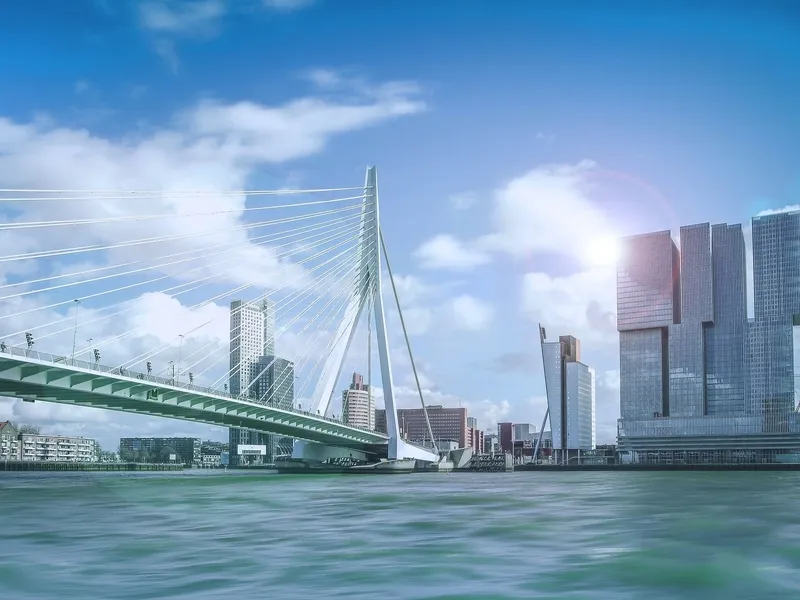 Stadtbild von Rotterdam mit Erasmusbrücke und modernen Gebäuden am Wasser.