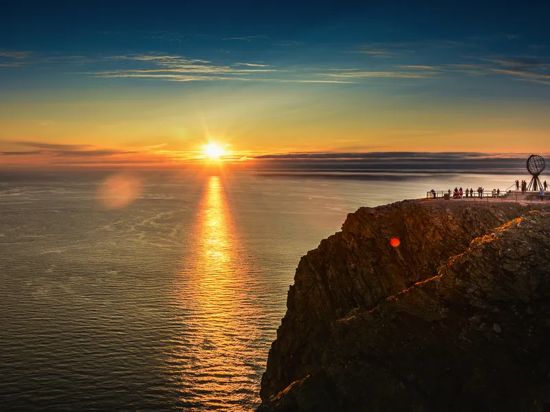Klippe bei Sonnenuntergang mit Menschen und Globus-Skulptur im Nordkap, Norwegen.
