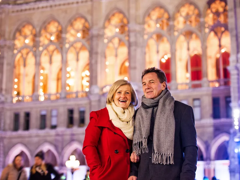Ein lächelndes Paar vor einem beleuchteten historischen Gebäude.