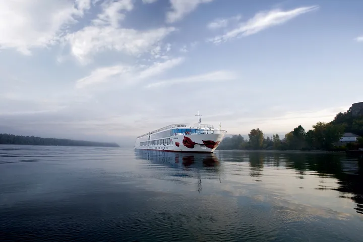 Ein großes weißes Kreuzfahrtschiff auf einem ruhigen Fluss mit bewaldeten Ufern.