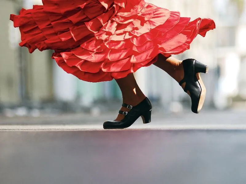 Tänzerin in roten Rock mit schwarzen Schuhen, die auf einer Straße Flamenco tanzt.