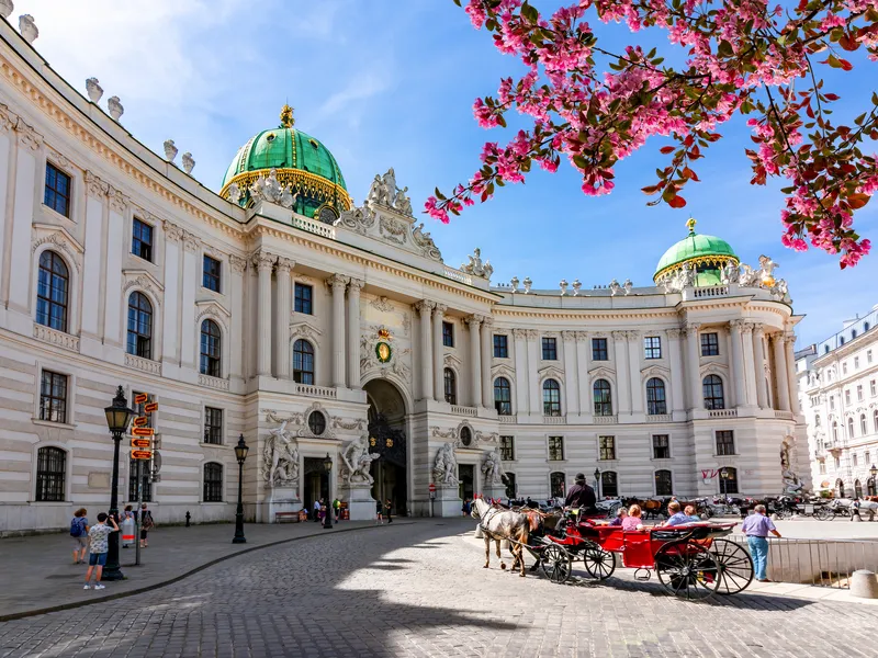 Hofburg Wien im Frühling mit Pferdekutsche und blühenden Bäumen.