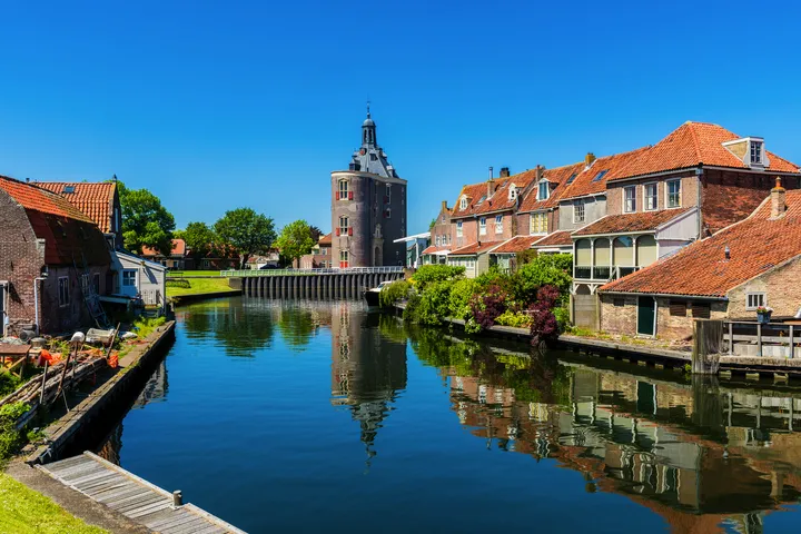 © allard1 - stock.adobe.com Historische Gebäude und ein Turm am Wasser mit klarem Himmel.
